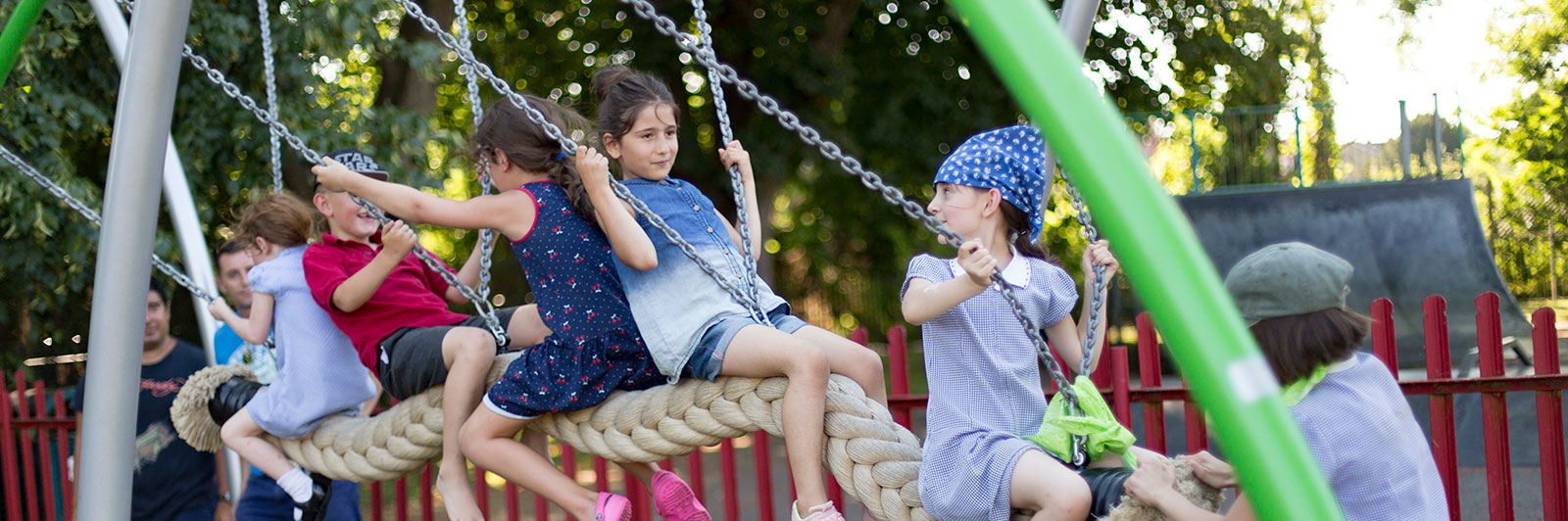 Lots of children swing on a long swing at a playground.